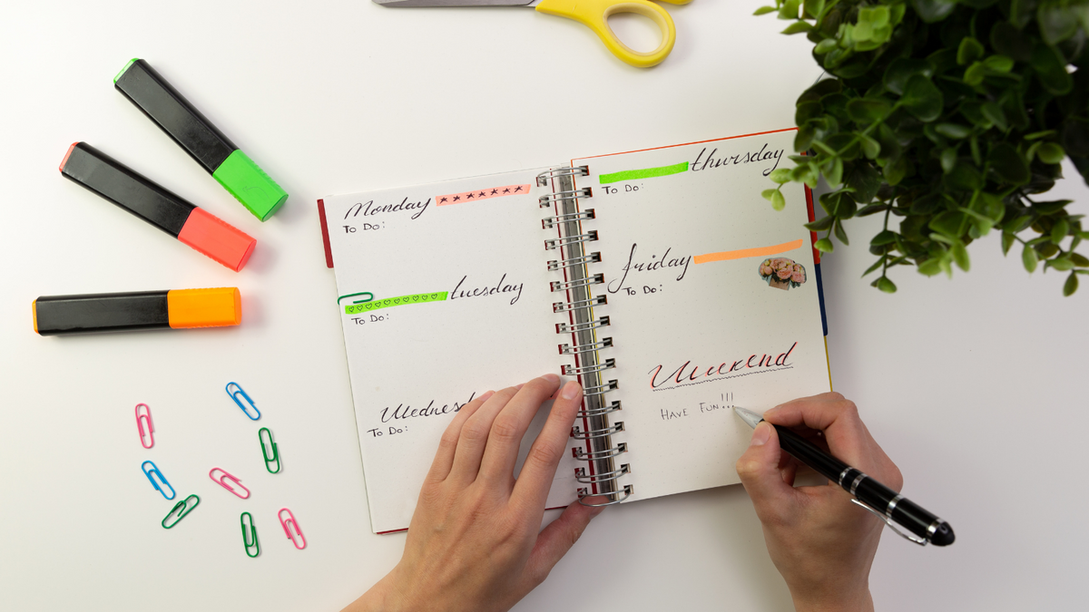 A person decorating their bullet journal with highlighters and colorful stickers.