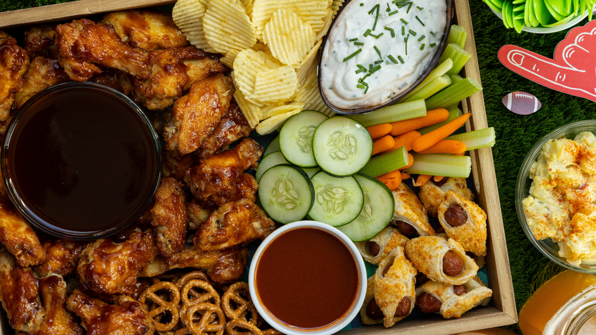 A table is set for a Super Bowl party, featuring wings, dips, chips, cucumbers, carrots, and celery among other delicious snacks.